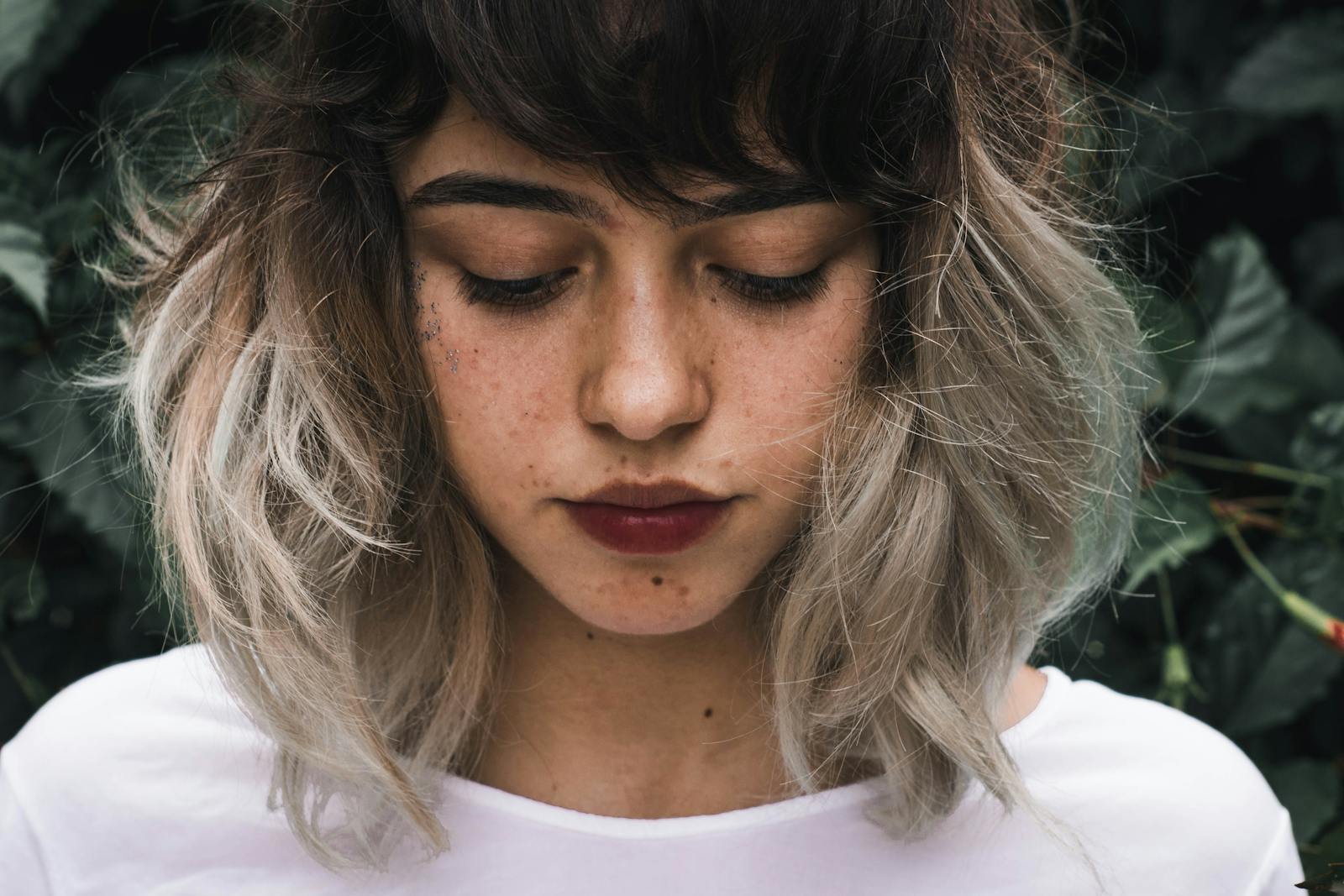 Close-up portrait of a young woman with freckles and two-toned hair outdoors.