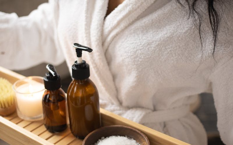 A woman in a bathrobe holds a tray of natural spa products, focusing on self-care.