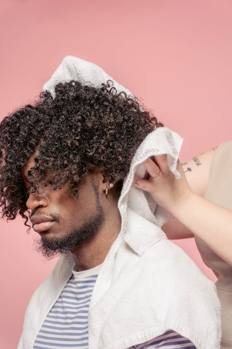 A man with curly hair getting styled by a professional hairdresser in a studio setting.